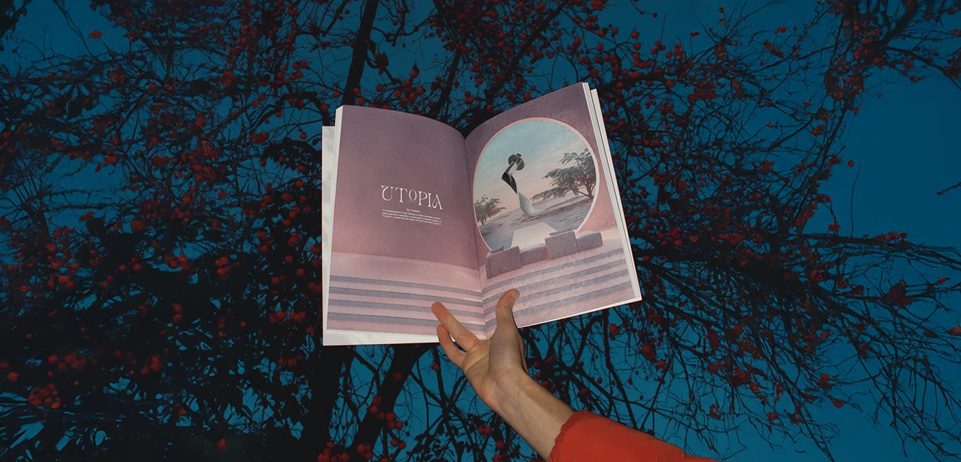 La revista abierta por Utopia, sostenida en alto contra un cielo azul y ramas con frutos rojos